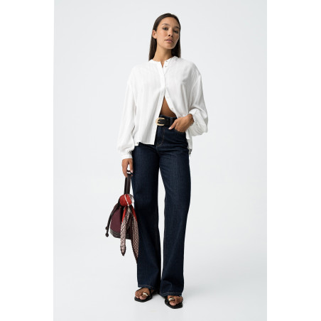 Blusa blanca de manga larga con rayas verticales y detalles brillantes. Botones frontales y puños elásticos.