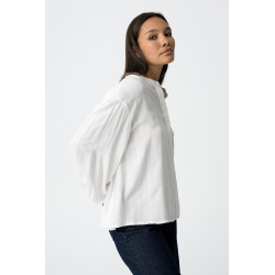Blusa blanca de manga larga con rayas verticales y detalles brillantes. Botones frontales y puños elásticos.