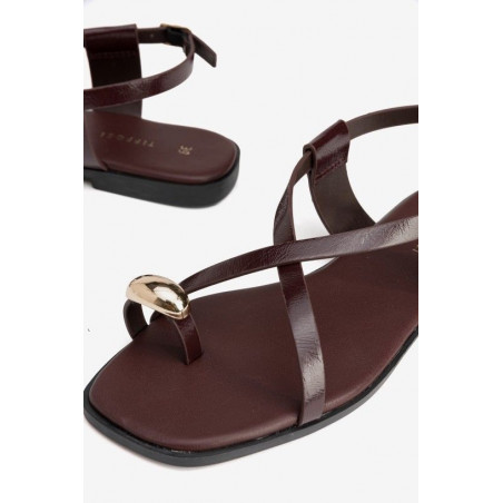 Sandalia plana con tiras finas cruzadas con detalle metálico dorado en la posición del dedo. Cierre hebilla lateral