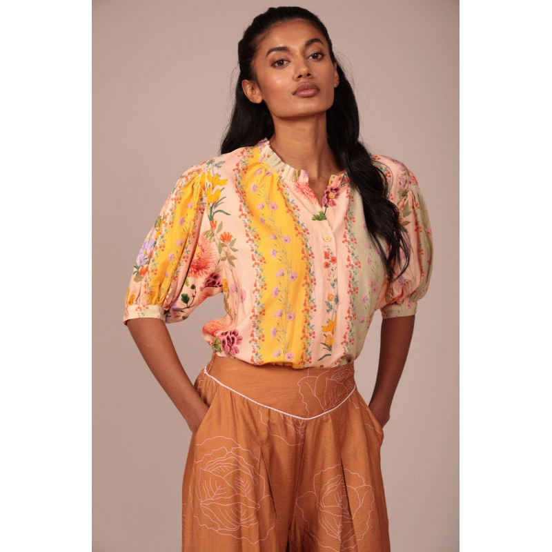 La prenda cuenta con un cuello fruncido con un pequeño volante que aporta un toque romántico y artesanal al escote. Su cierre fr