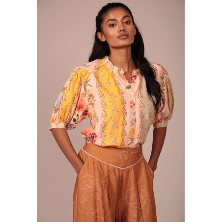 La prenda cuenta con un cuello fruncido con un pequeño volante que aporta un toque romántico y artesanal al escote. Su cierre fr