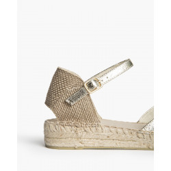 Alpargata de cuña baja, acabado dorado metalizado, caracterizada por su suela de yute trenzado y cierre de pulsera hebilla