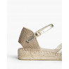 Alpargata de cuña baja, acabado dorado metalizado, caracterizada por su suela de yute trenzado y cierre de pulsera hebilla
